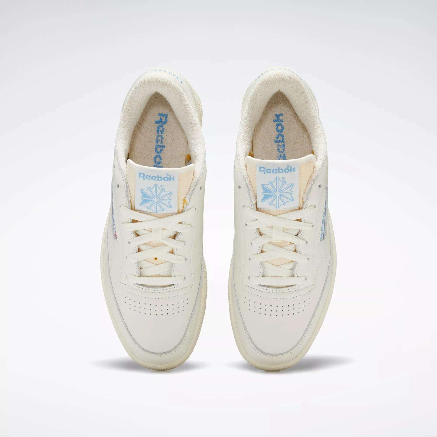 A pair of Club C 85 Vintage Shoes by Reebok, seen from above, with an off-white leather upper, light blue Reebok branding on the tongue and side, cream laces, and a soft textured inner lining.