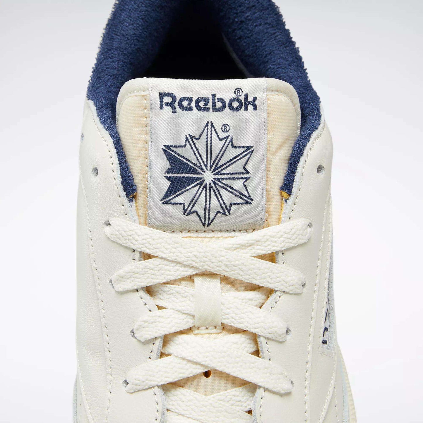 Close-up of the Reebok Club C 85 Vintage Shoes featuring a cream-colored leather upper, white laces, signature Reebok logo, star design on the tongue, and dark blue inner lining for lightweight cushioning and all-day comfort.