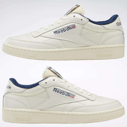 The Reebok Club C 85 Vintage Shoes are shown side view against a white background, featuring a durable white leather upper, navy blue lining, and the iconic Reebok logo with a small Union Jack flag on each side.
