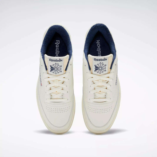 Top view of a pair of Reebok Club C 85 Vintage Shoes in off-white with a leather upper, navy blue inner lining, perforated toe boxes, and Reebok logo with star on the tongues.