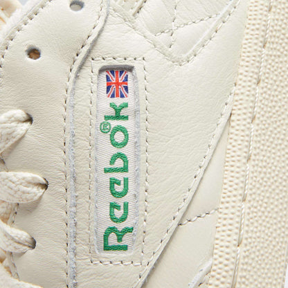 Close-up of Reebok Women's Club C 85 Vintage Shoes in white, showcasing the stitched green Reebok logo with a small Union Jack, white laces, and premium textured leather.