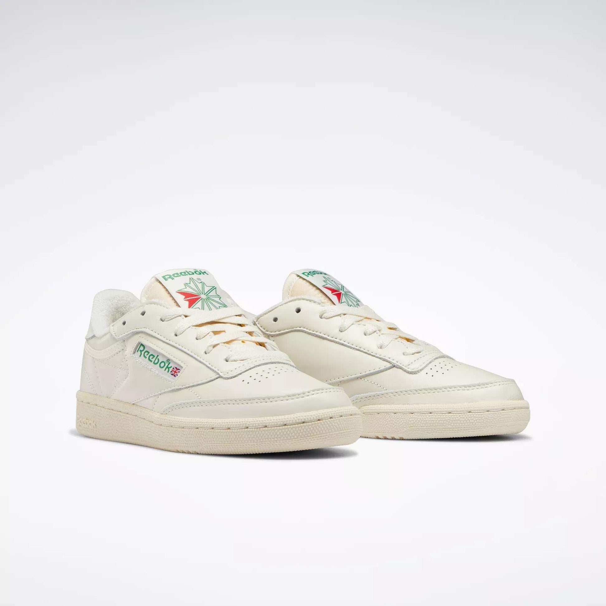 A pair of off-white Reebok Women's Club C 85 Vintage Shoes with green and red logo details, shown against a plain light background. These classic low-top tennis shoes feature perforated toes and durable rubber soles.