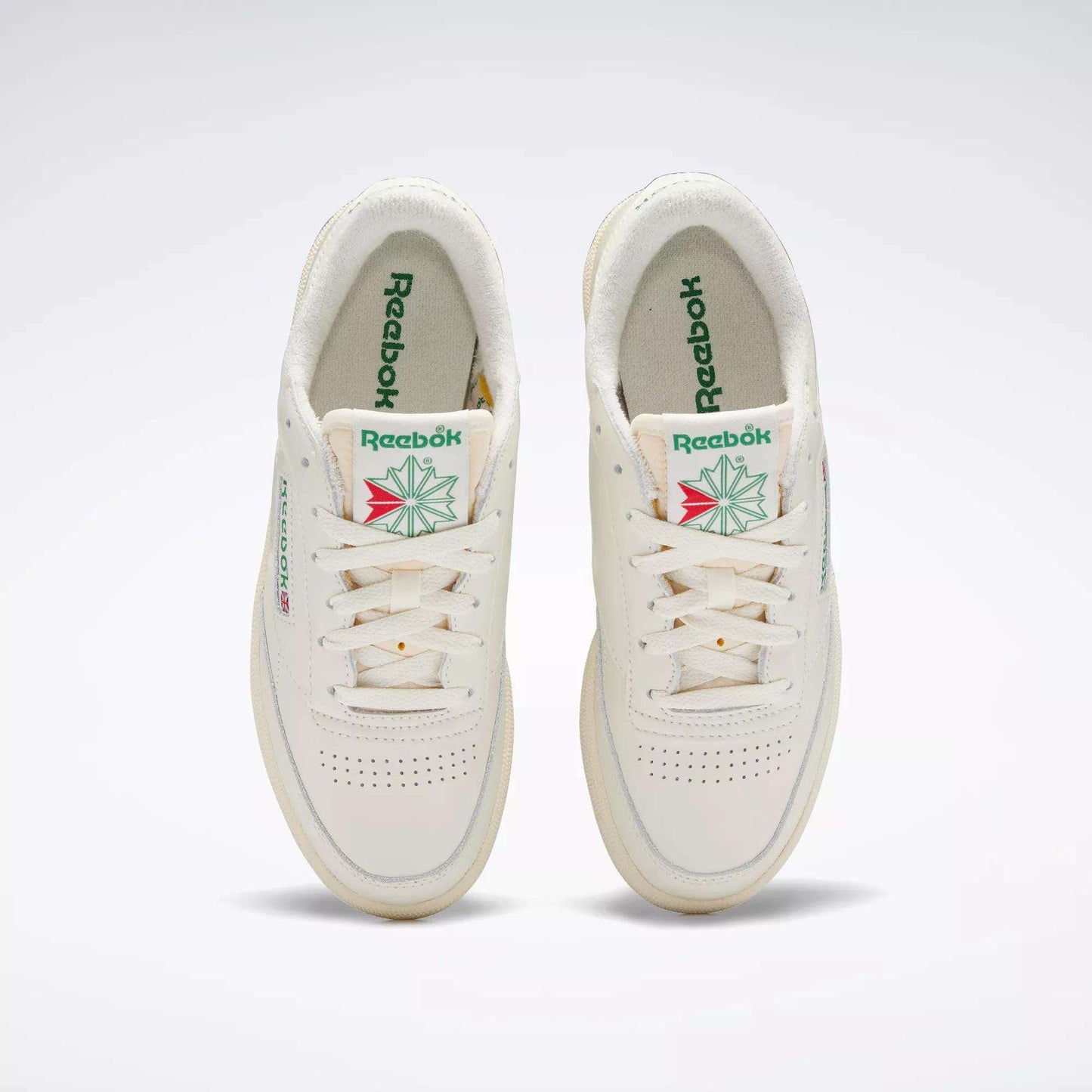 A pair of off-white Reebok Women's Club C 85 Vintage Shoes with green Reebok branding and a geometric floral design on the tongue, viewed from above on a plain background.