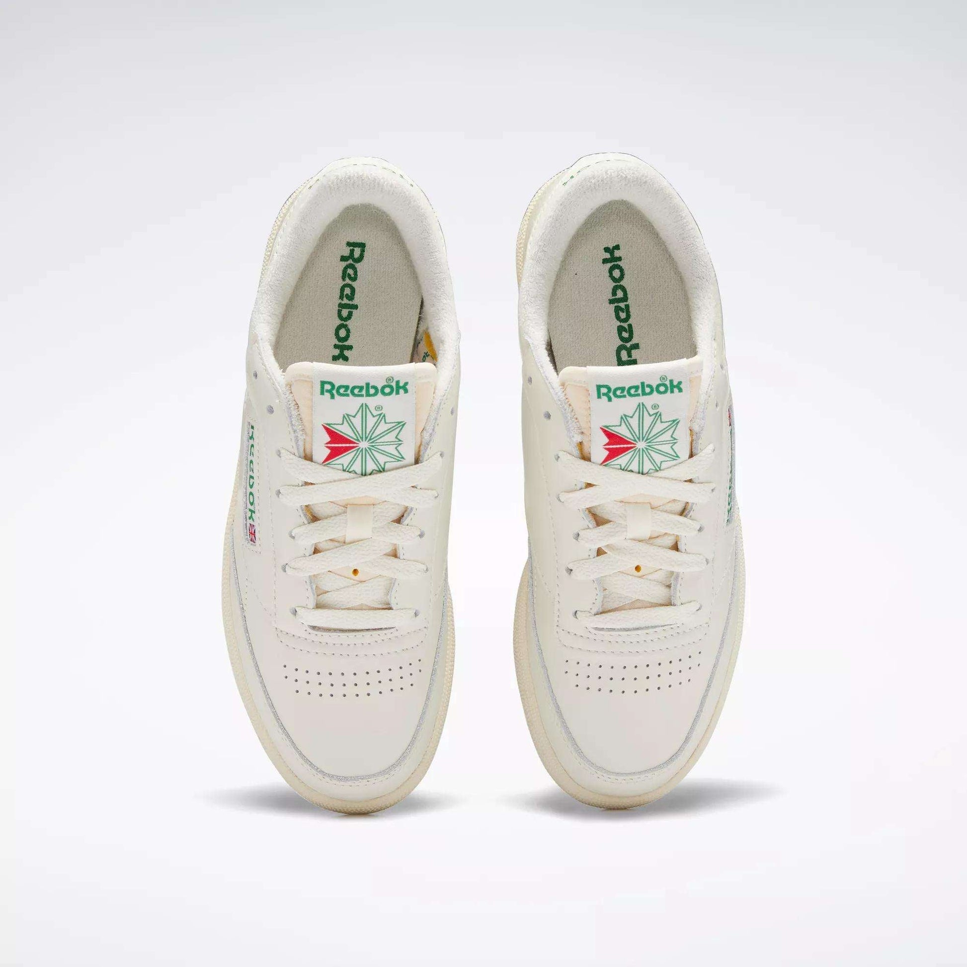 A pair of off-white Reebok Women's Club C 85 Vintage Shoes with green Reebok branding and a geometric floral design on the tongue, viewed from above on a plain background.