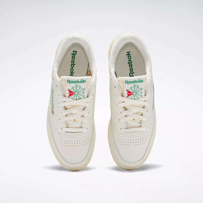 A pair of off-white Reebok Women's Club C 85 Vintage Shoes with green Reebok branding and a geometric floral design on the tongue, viewed from above on a plain background.