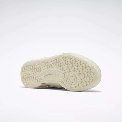 A Women's Club C 85 Vintage Shoe by Reebok rests on its side, showcasing a textured sole with a circular grip and an embossed Reebok logo at the center. This tennis-inspired sneaker pops against a light gray background.