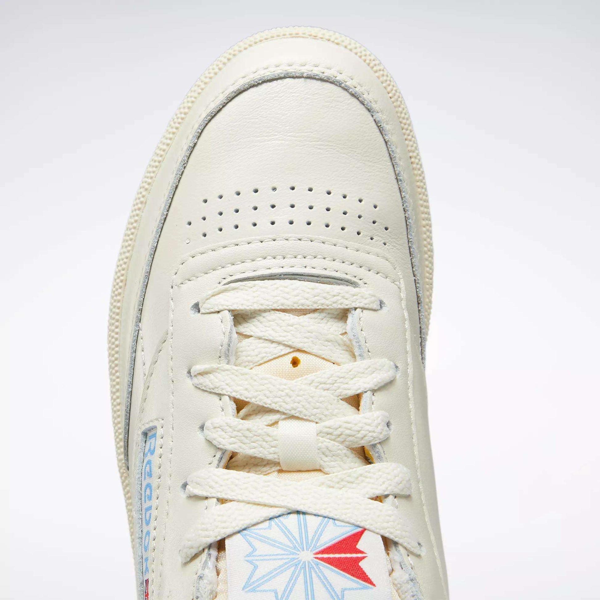Close-up of the Reebok Women's Club C 85 Vintage Shoes in cream leather, tennis-inspired with a perforated toe box, white laces, and a blue and red Reebok logo on the tongue.