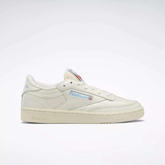 A side view of Reebok Women's Club C 85 Vintage Shoes, featuring an off-white tennis-inspired design with light blue and red branding accents and a cream sole, displayed on a plain white background.