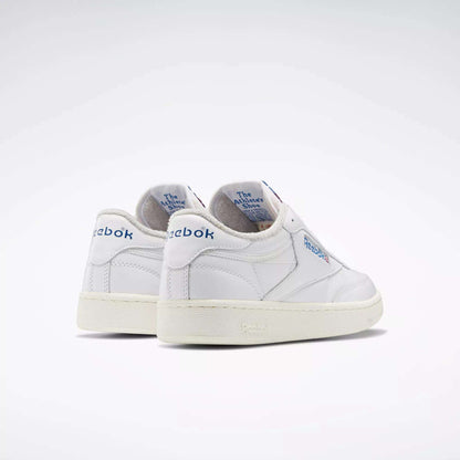 A pair of Reebok Club C 85 Vintage Shoes in white with blue branding and lightweight cushioning, featuring The Animals Observatory text on the inner heel, displayed against a plain, light background.