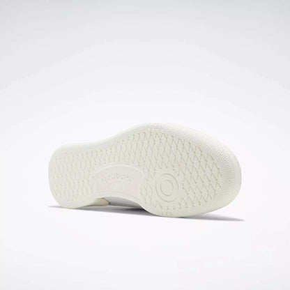 The Reebok Club C 85 Vintage Shoe in white is pictured on its side, revealing a textured sole with a circular pattern and an embossed Reebok logo, set against a plain light gray background.