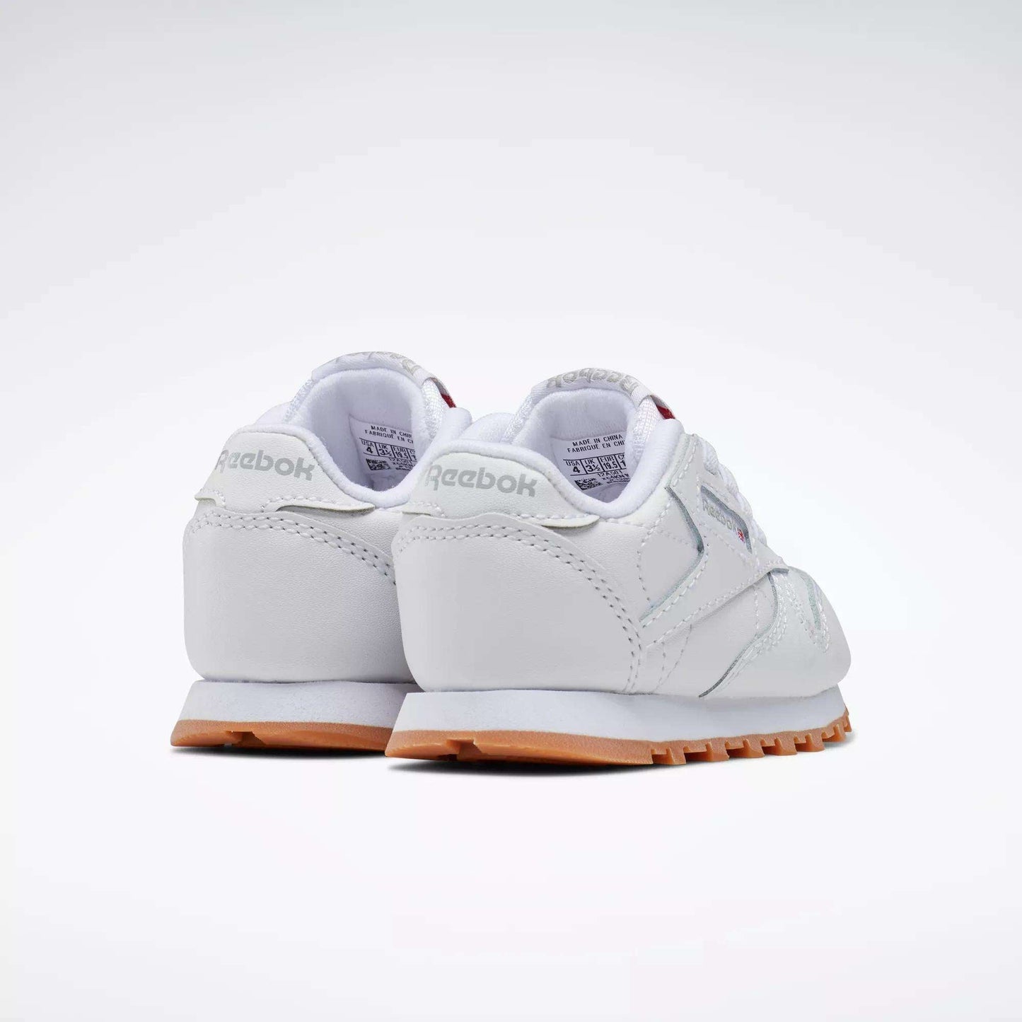 The Reebok Kids' Classic Leather Shoes - Baby & Toddler in white with light gray accents and gum soles are shown from the back and side on a plain white background. Ideal for toddlers who enjoy timeless style.