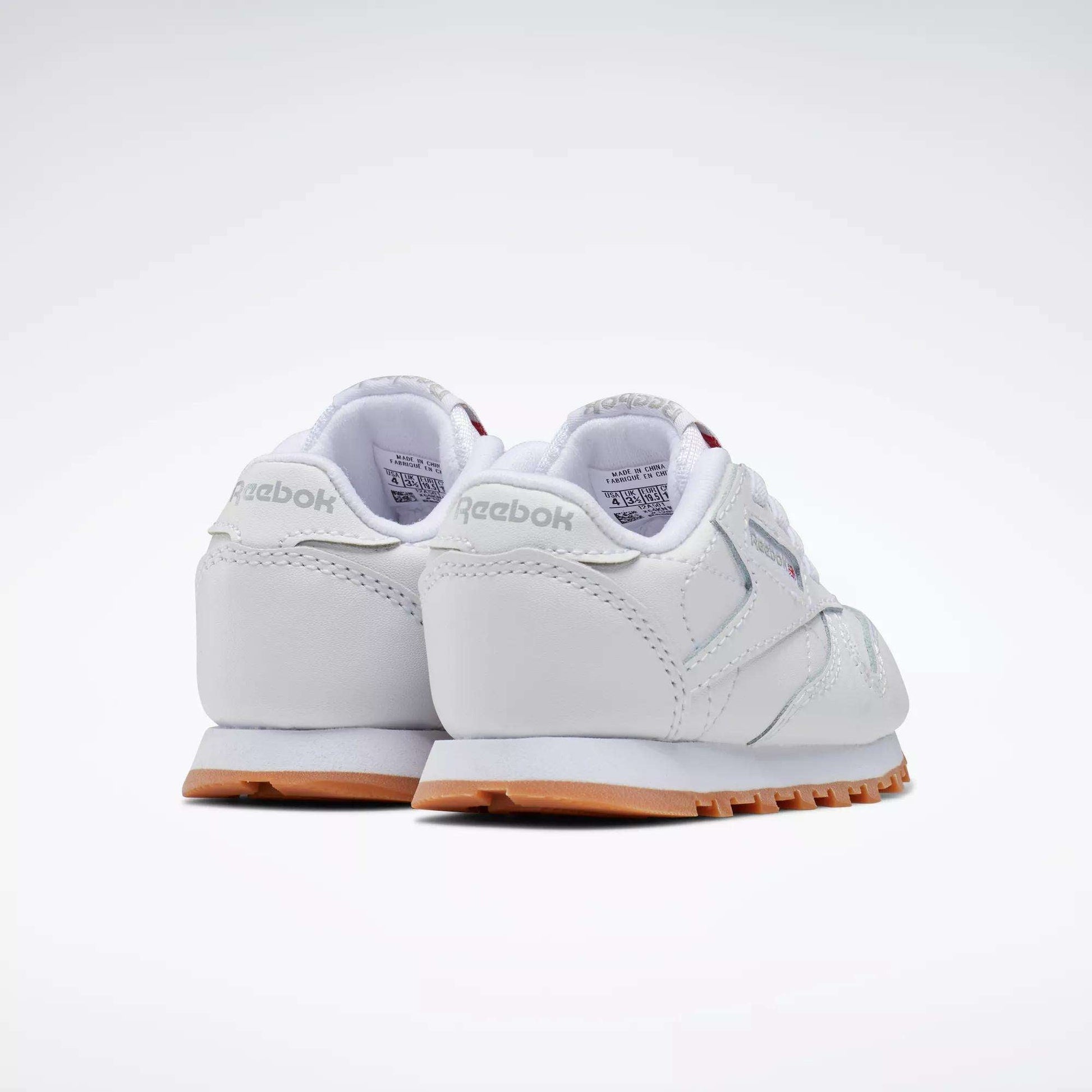 The Reebok Kids' Classic Leather Shoes - Baby & Toddler in white with light gray accents and gum soles are shown from the back and side on a plain white background. Ideal for toddlers who enjoy timeless style.