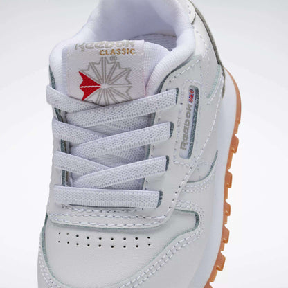 Close-up of Reebok Kids' Classic Leather Shoes - Baby & Toddler, featuring white leather, logo on tongue, laces, perforated toe, stitched details, and a gum outsole—ideal for toddler style and comfort.