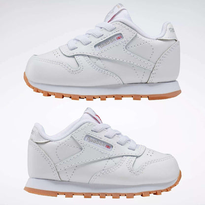 The Reebok Kids' Classic Leather Shoes - Baby & Toddler are white with white laces, light brown rubber soles, and display the iconic Reebok logo with a small UK flag on the side.