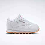 The Reebok Kids' Classic Leather Shoes for babies and toddlers are white with a light brown sole, white laces, and a side tag featuring the Reebok logo, shown from the side on a plain white background.