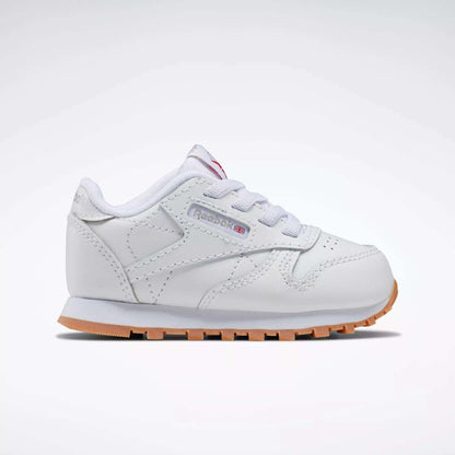 The Reebok Kids' Classic Leather Shoes for babies and toddlers are white with a light brown sole, white laces, and a side tag featuring the Reebok logo, shown from the side on a plain white background.