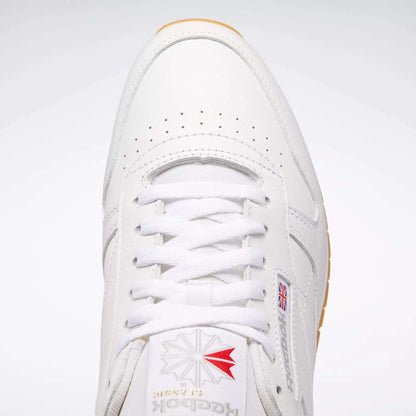 Top view of Reebok Classic Leather Shoes featuring white laces, durable leather, perforated toe detailing, a red and grey logo on the tongue, and a small Union Jack flag on the side for retro style.