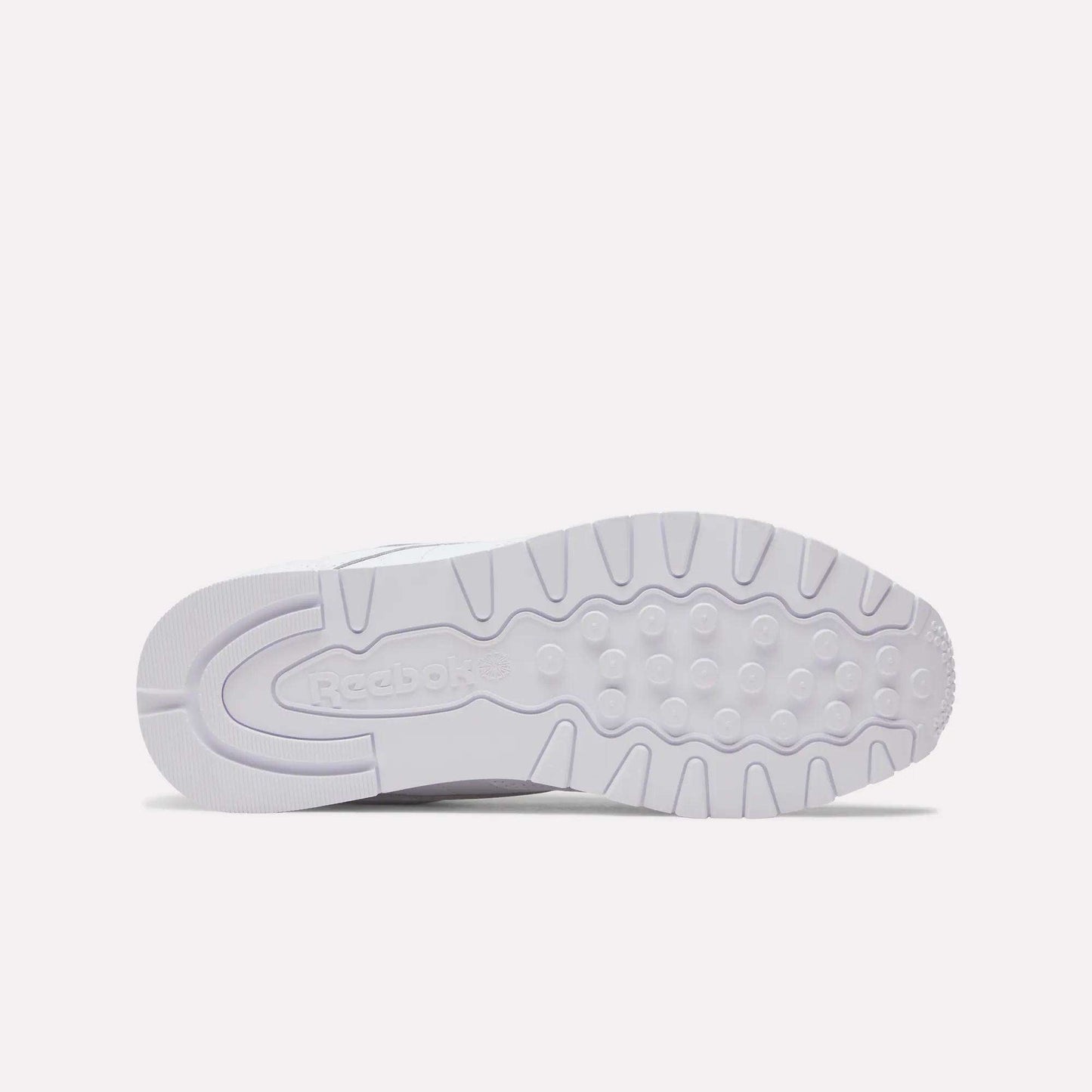 The image displays the white rubber outsole of Reebok Classic Leather Shoes from below, showing the Reebok logo and circular grip patterns—a stylish detail for these retro-inspired sneakers.