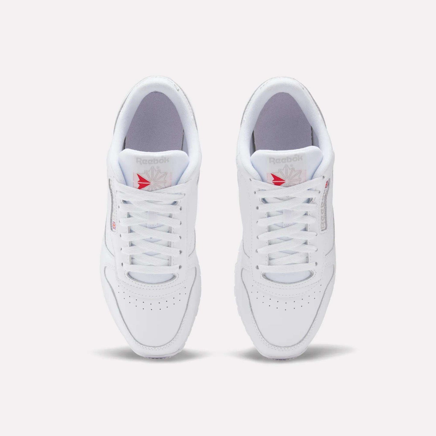 A top view of Reebok Classic Leather Shoes shows a leather upper with laces, perforated toes, and red Reebok logos on the tongues, offering a timeless retro style.