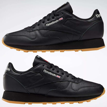 Two black Reebok Classic Leather Shoes with durable leather uppers and tan rubber soles, shown from the side. The Reebok logo and Union Jack are displayed near the laces.
