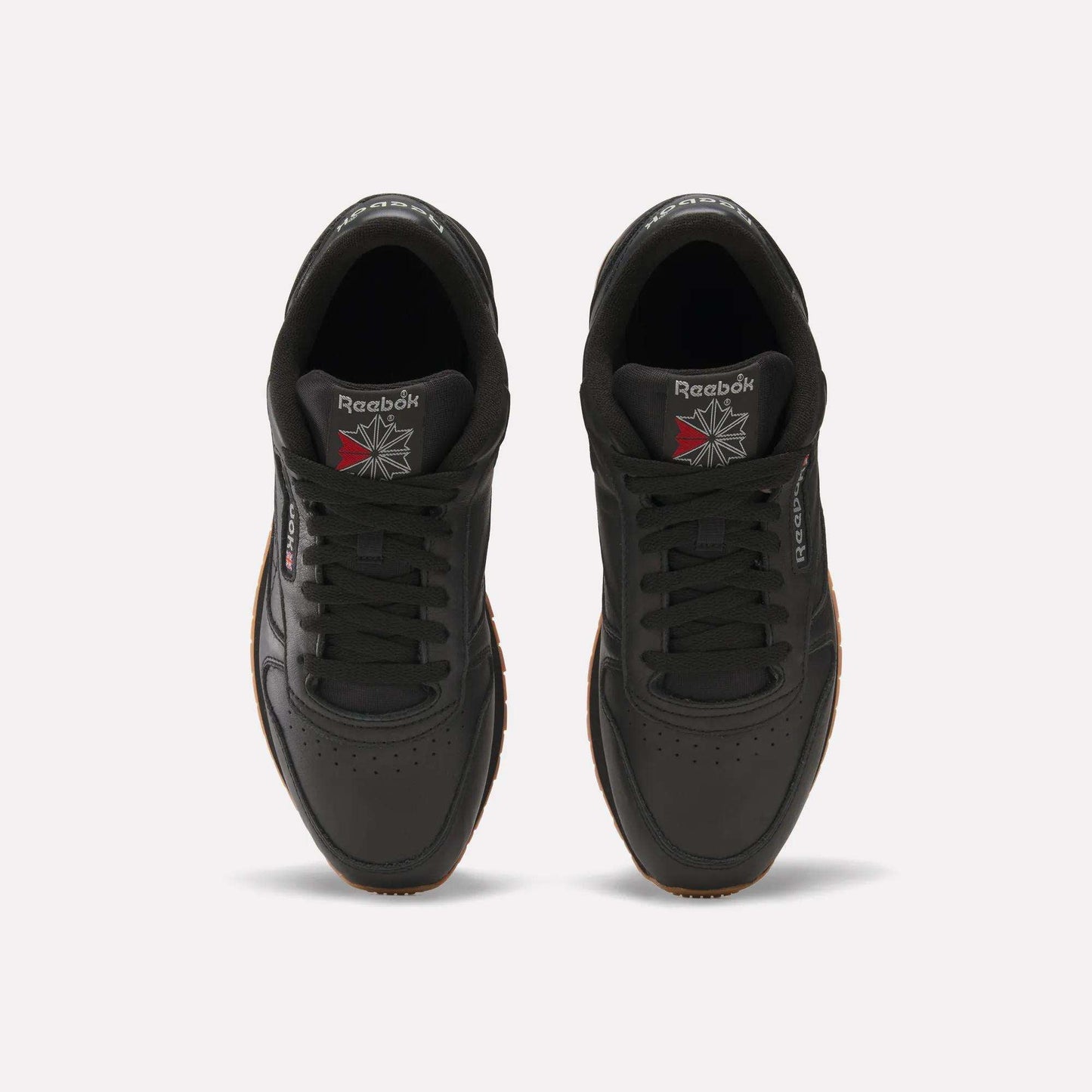 Top view of a pair of Reebok Classic Leather Shoes in black with black laces, gum soles, and the Reebok logo on the tongues and sides. Durable leather and retro design stand out against a white background.