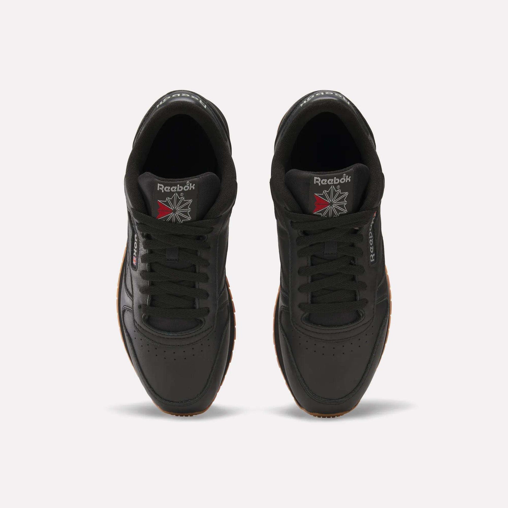 Top view of a pair of Reebok Classic Leather Shoes in black with black laces, gum soles, and the Reebok logo on the tongues and sides. Durable leather and retro design stand out against a white background.