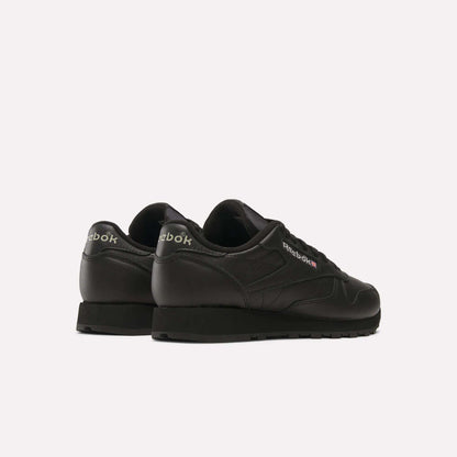 A pair of Reebok Classic Leather Shoes with a black leather upper are displayed on a white background, angled to reveal retro Reebok branding on the heels and sides.