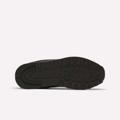 A bottom view of the Reebok Classic Leather Shoes in black shows a textured rubber outsole with circular and linear tread and the Reebok logo near the heel—retro-inspired style.