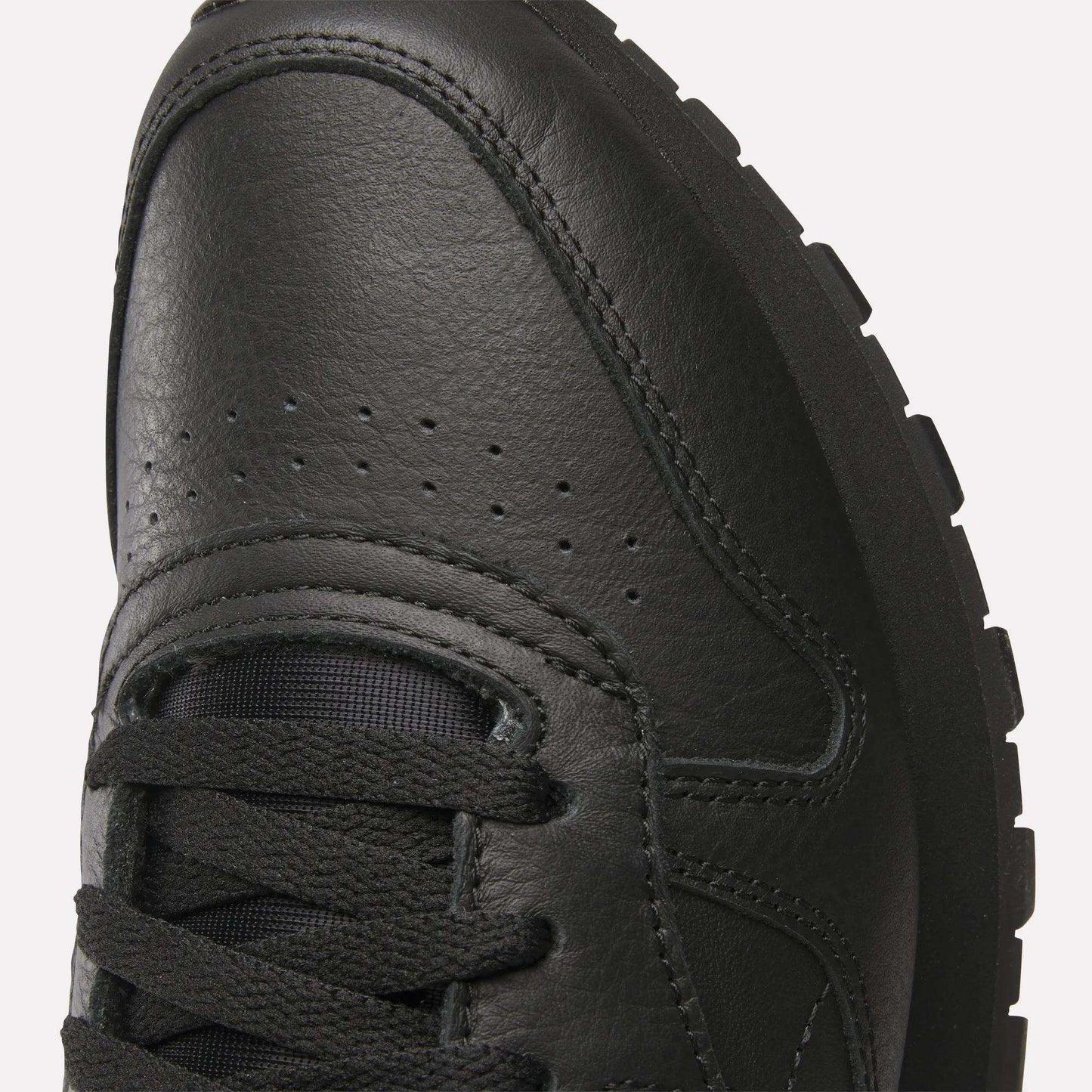 Close-up of the toe and laces of Reebok Classic Leather Shoes, highlighting stitching, ventilation perforations, and textured rubber sole for a retro-inspired look with a durable leather upper.