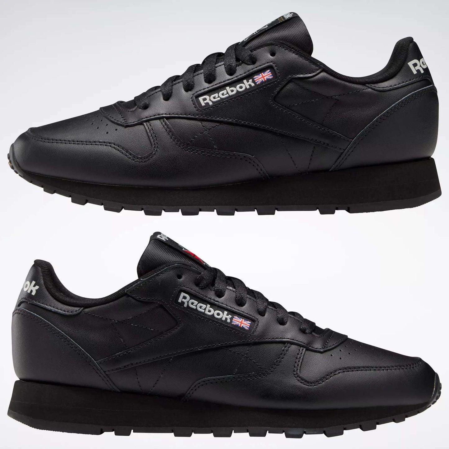 Two Reebok Classic Leather Shoes in black are displayed side by side on a white background, featuring the Reebok logo and British flag near the laces, minimalist stitching, and black rubber soles.