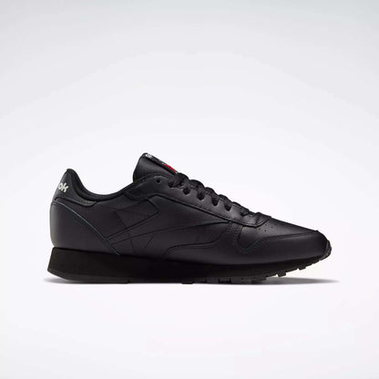 A side profile of the Reebok Classic Leather Shoes is shown on a white background, featuring a sleek black design with matching laces, stitching accents, and a durable leather trainer sole.