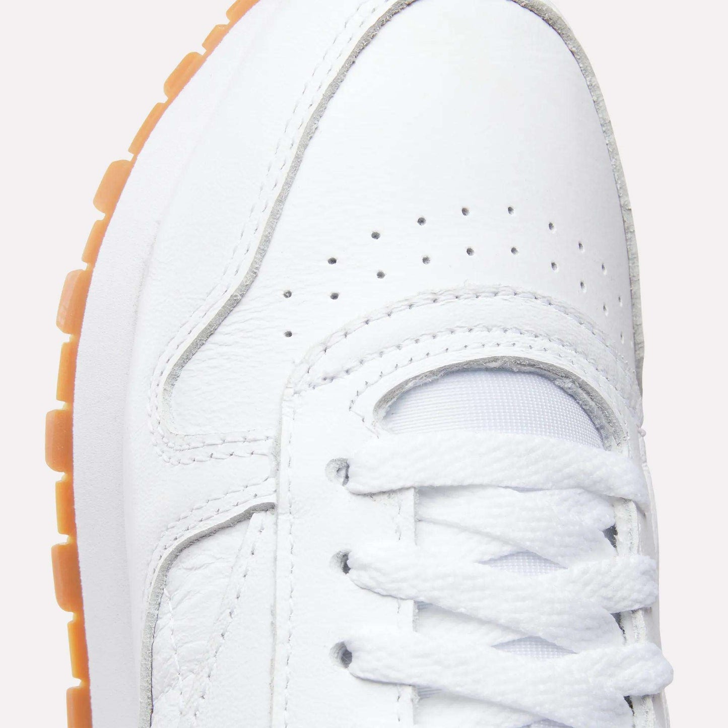 Close-up of the toe and laces on Reebok Women's Classic Leather Shoes, featuring perforated toe box, white stitching, cushioned midsole for comfort, and a gum rubber sole.
