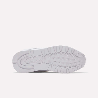 The image displays the outsole of a Women's Classic Leather Shoe by Reebok, featuring white rubber with grooves, circular treads, and an embossed Reebok logo near the heel. The sneaker is shown lying on its side.