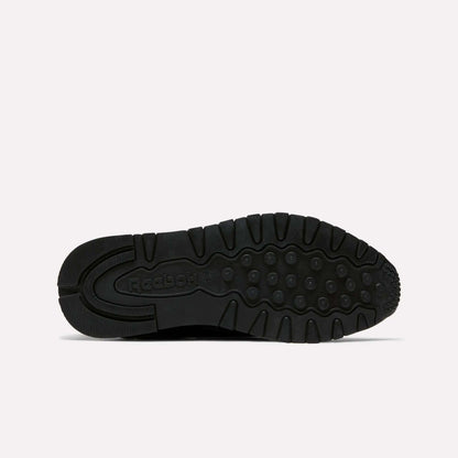 The image shows the black rubber sole of the Reebok Women's Classic Leather Shoes, viewed from below. It features circular tread patterns, grooves for traction, Reebok branding near the heel, and a cushioned midsole for comfort.