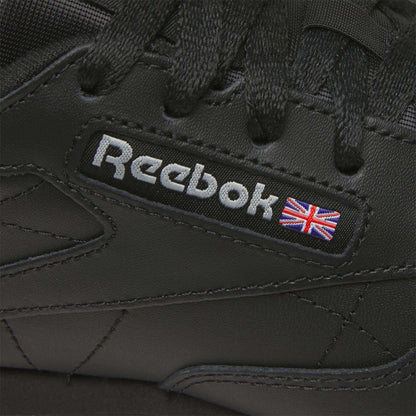 Close-up of Reebok Women's Classic Leather Shoes in black, showcasing the Reebok logo, a small Union Jack flag by the laces, and a cushioned midsole for comfort.