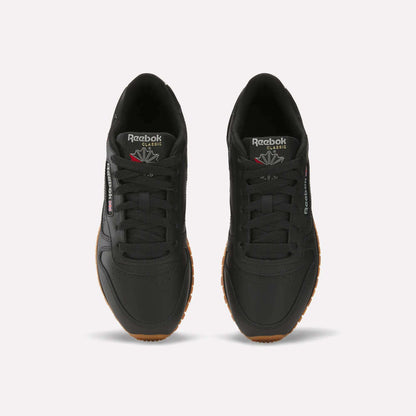 A pair of Women's Classic Leather Shoes by Reebok in black with gum soles, shown from above. They display the Reebok logo on the tongue and side, feature cushioned midsoles, and have neatly tied laces for comfort and style.
