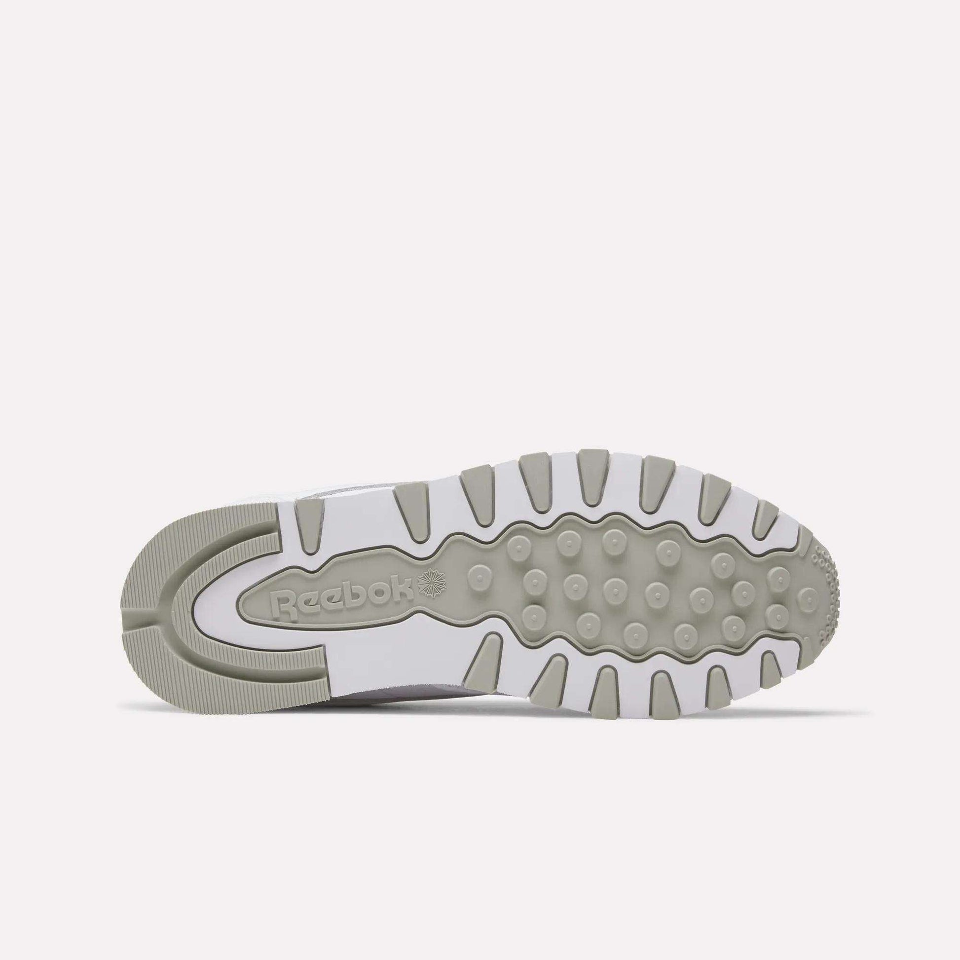 The image displays the sole of Reebok Classic Leather Shoes, combining light gray and white hues with textured grips and the Reebok logo embossed near the heel.