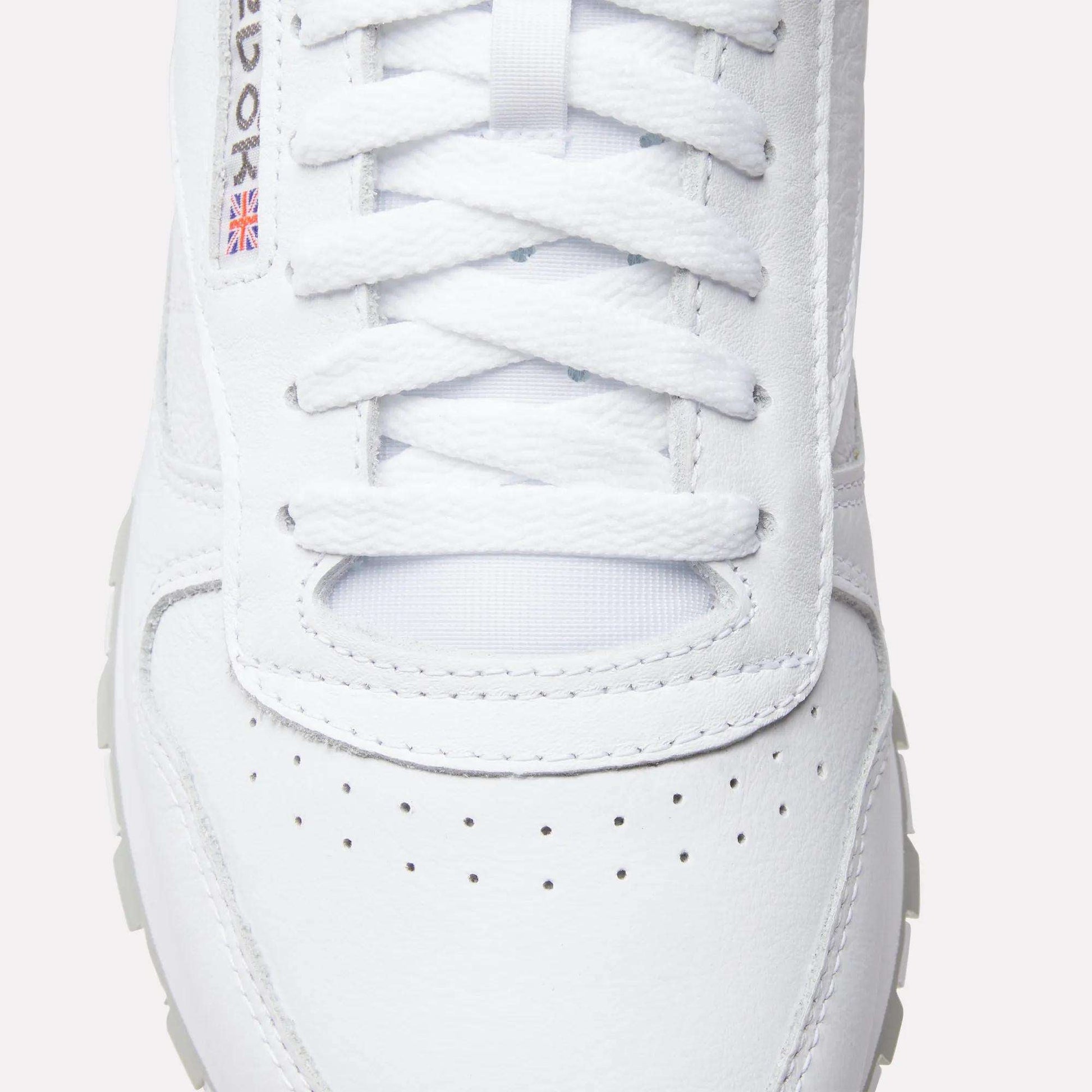 Close-up of Reebok Classic Leather Shoes with laces, a perforated toe box, textured leather, and a small Union Jack flag detail by the eyelets—iconic elements from Reebok’s retro design.