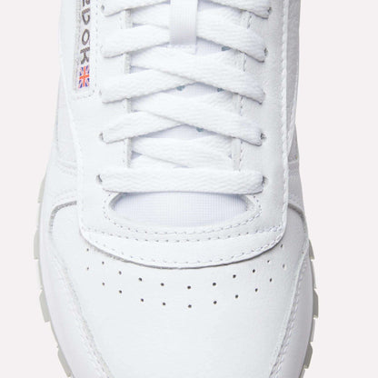 Close-up of Reebok Classic Leather Shoes with laces, a perforated toe box, textured leather, and a small Union Jack flag detail by the eyelets—iconic elements from Reebok’s retro design.