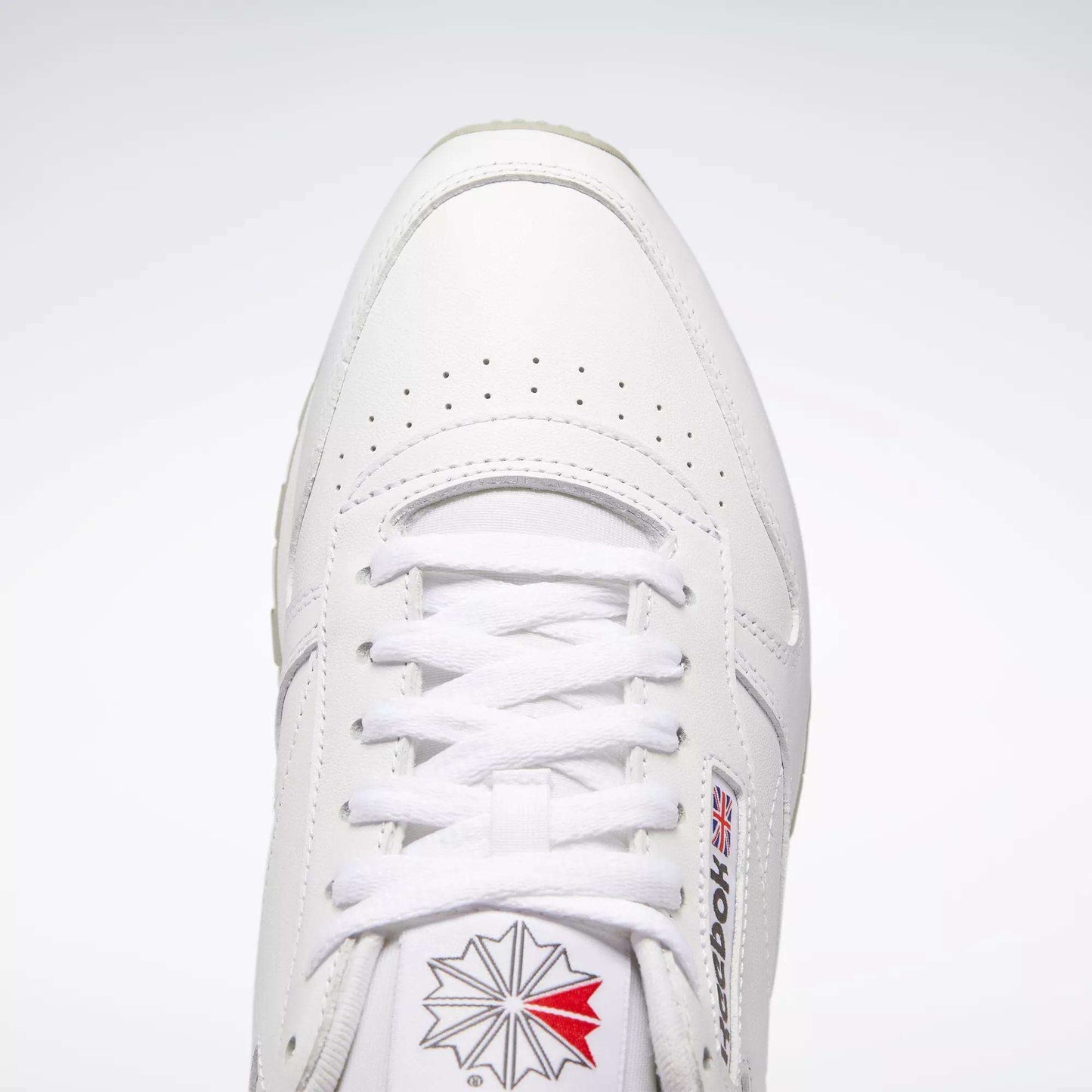 Top view of Reebok Classic Leather Shoes in white, retro style with durable leather, white laces, toe perforations, and the Reebok logo with British flag on the side and tongue against a light background.