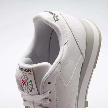 A close-up of the Reebok Classic Leather Shoes highlights their retro style, white leather upper, minimalist design, light gray sole accents, and signature tongue with Reebok logo and star graphic.
