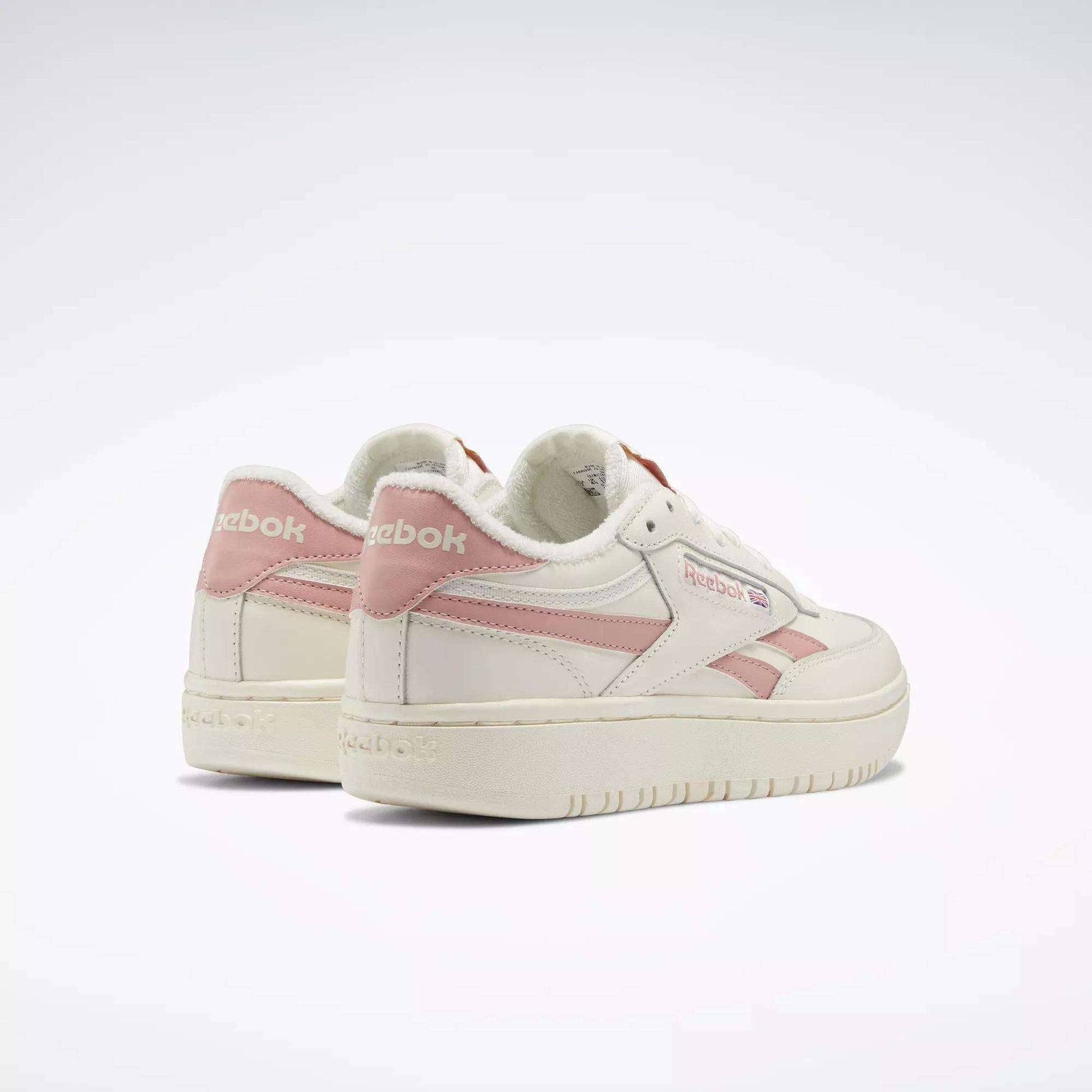 A pair of Reebok Women's Club C Double Revenge Shoes in white and pale pink are displayed on a plain white background—one shoe faces forward, while the other shows off the heel and Reebok side logo.