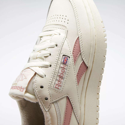 Close-up of Reebok Women's Club C Double Revenge Shoes in cream with pink accents, leather upper, Reebok logo, Union Jack flag on the side, cream laces, textured sole, and court-inspired design details.