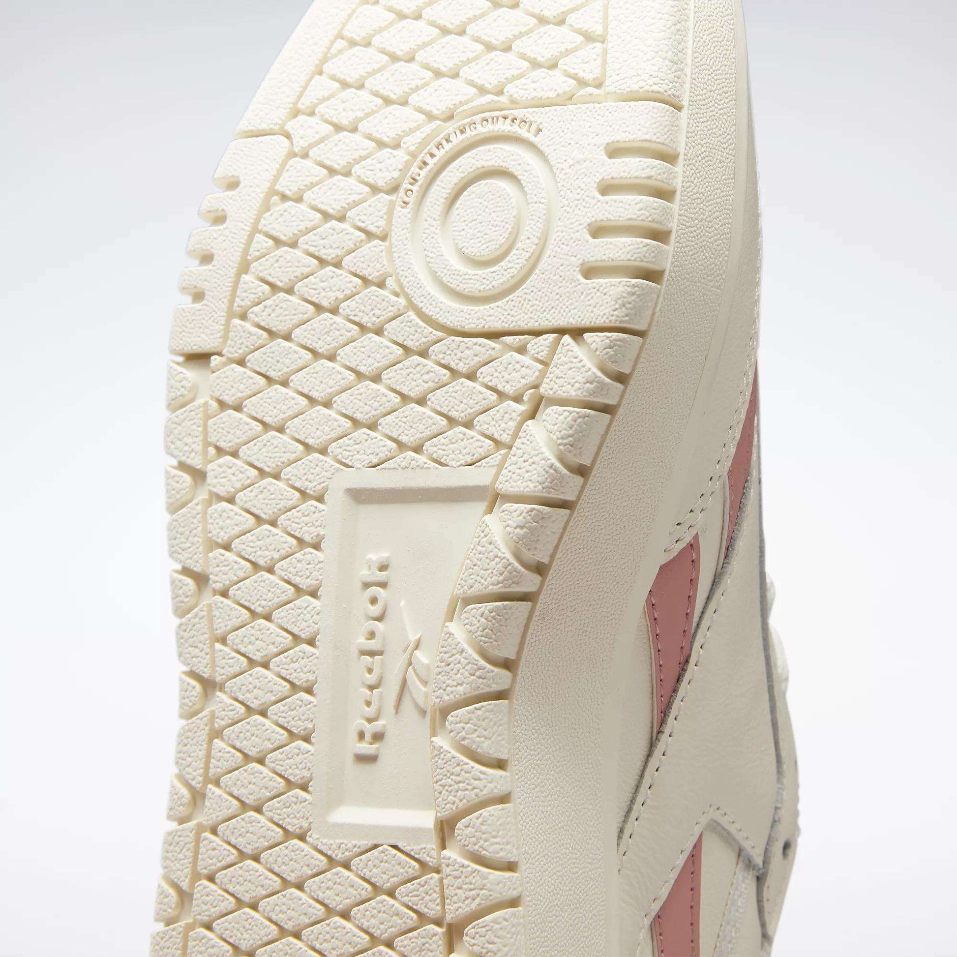 Close-up of the off-white rubber outsole on Reebok Women's Club C Double Revenge Shoes, highlighting the textured tread, Reebok logo, and a glimpse of the shoe’s side with pink stripe detailing.