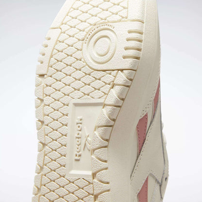 Close-up of the off-white rubber outsole on Reebok Women's Club C Double Revenge Shoes, highlighting the textured tread, Reebok logo, and a glimpse of the shoe’s side with pink stripe detailing.