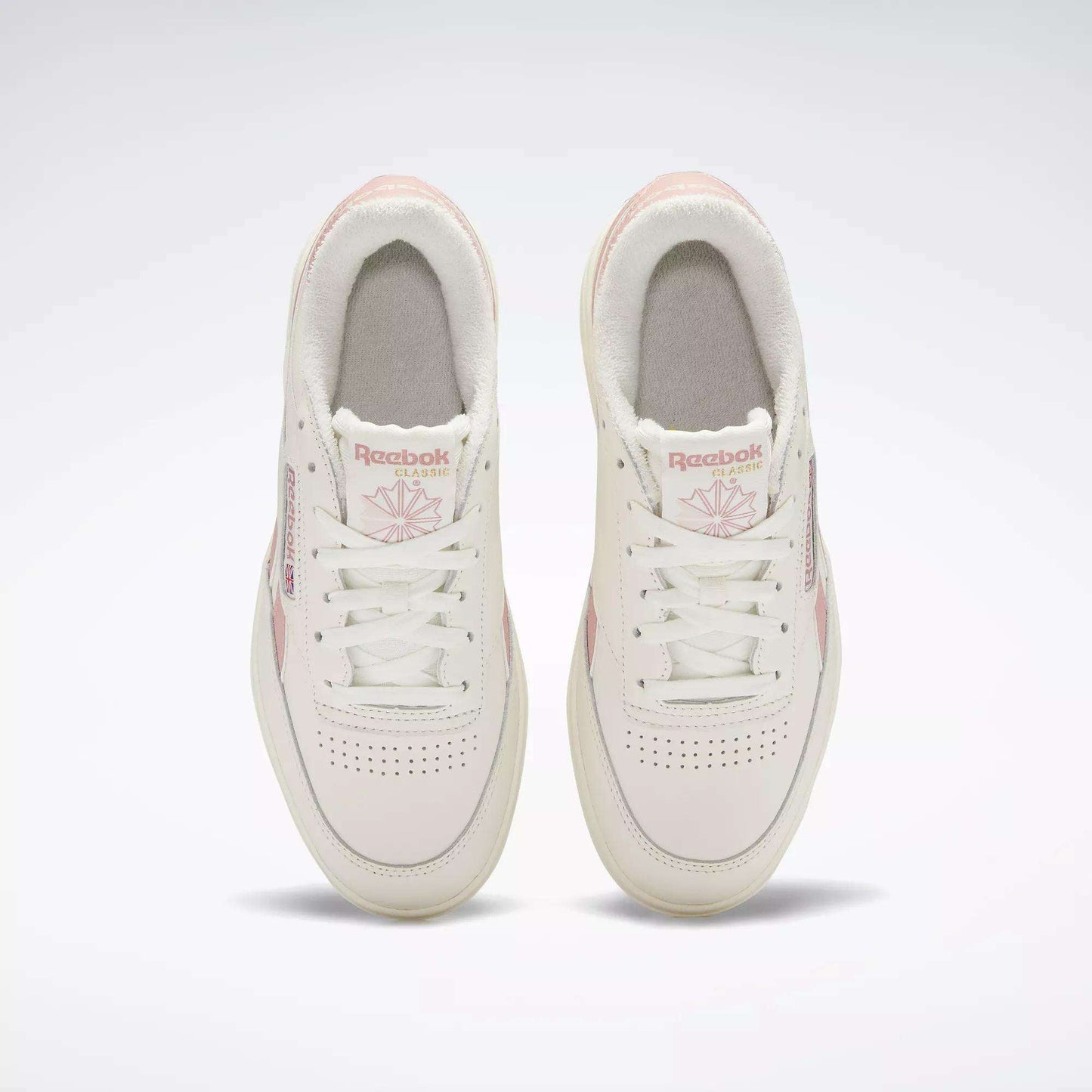 Top view of a pair of Reebok Women's Club C Double Revenge Shoes in white with light pink accents and laces, featuring the Reebok logo and design details on the tongues and sides, set against a plain white background.