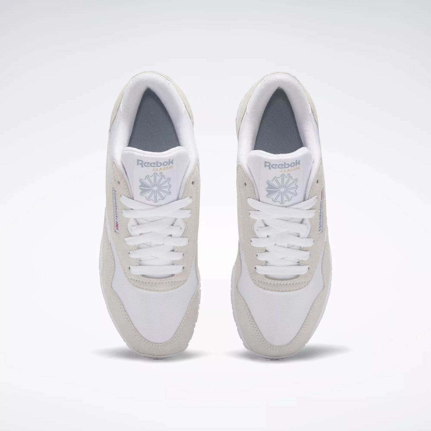 A pair of Women's Classic Nylon Shoes by Reebok, white with light gray accents, is shown from above on a plain background. These sneakers have white laces, a gray insole, and display the Reebok logo on the tongue and side.