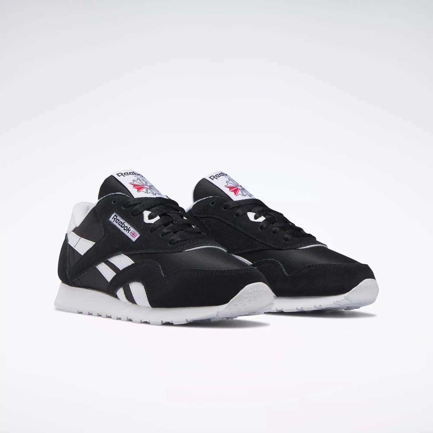 A pair of Women's Classic Nylon Shoes by Reebok in black suede with white soles, side stripes, and tongue labels showing the Reebok logo and Union Jack, ideal as everyday sneakers and shown on a plain white background.