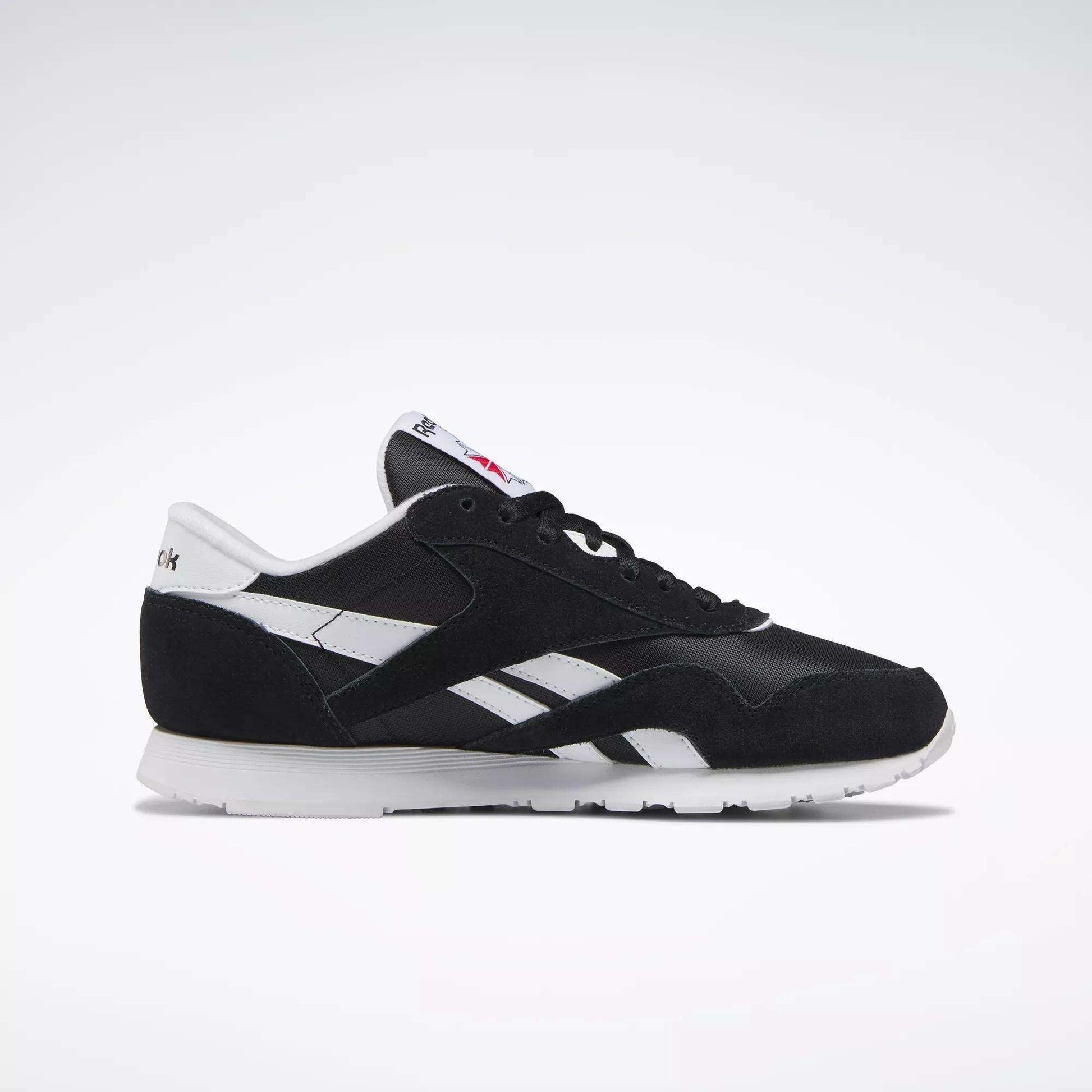 The Reebok Women's Classic Nylon Shoes feature a black upper, white side stripes, suede accents, and a white sole with logo details—shown in side profile on a light background. Stylish and comfortable sneakers for everyday wear.