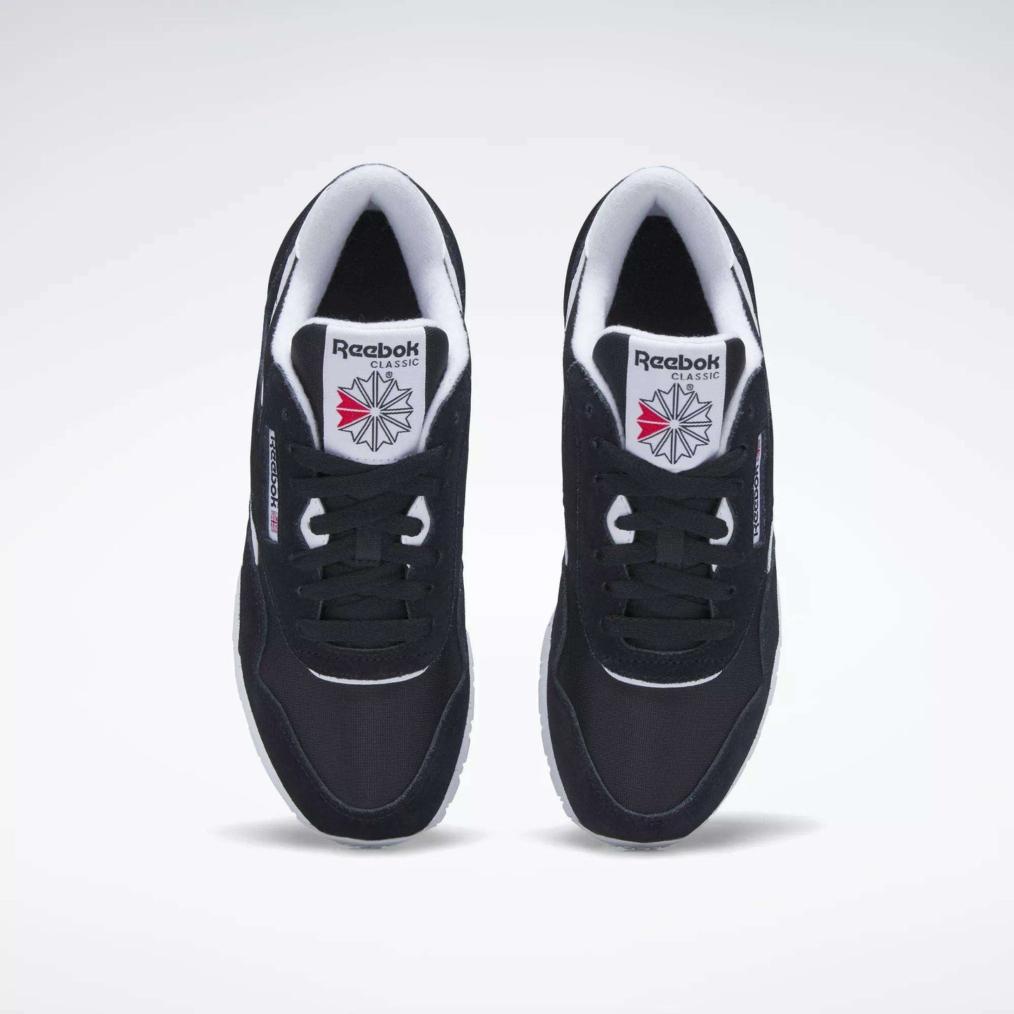 A top view of black Reebok Women's Classic Nylon Shoes with white soles and inner lining, featuring the Reebok logo and a red-and-grey starburst design on the tongue.